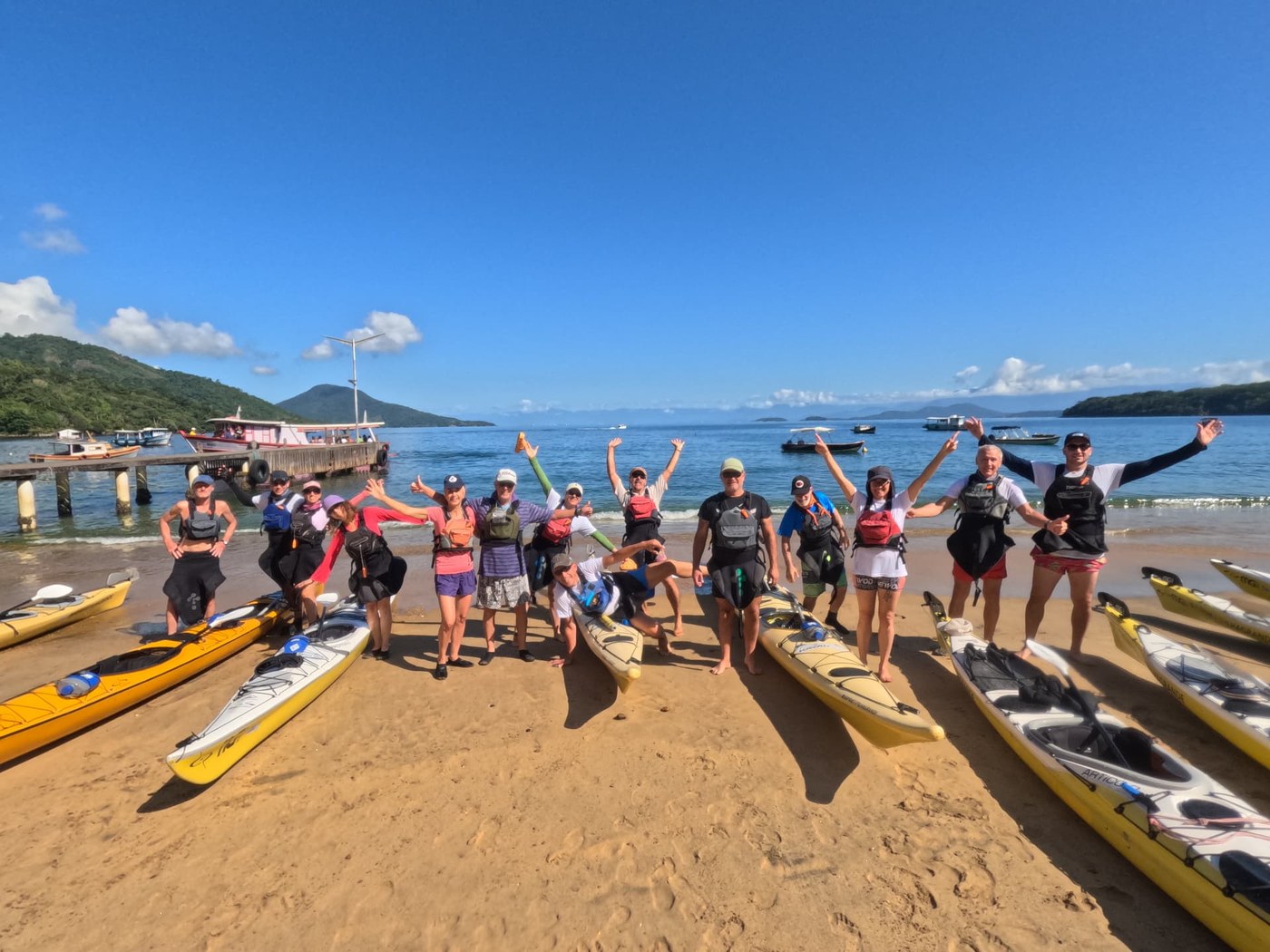 Grupo de kayakistas na praia, com seus caiaques e o mar ao fundo